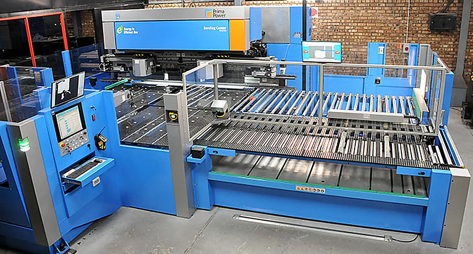 Blauwe CNC plaatbewerkingsmachine met rollenbaan, veiligheidshek en bedieningspaneel in een fabriekshal voor metaalbewerking.